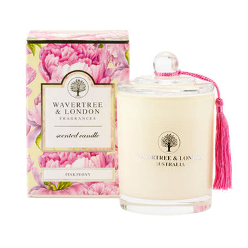 A glass candle in a light cream colour next to a box illustrated with pink peony flowers.