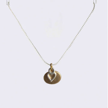 A chain necklace with a hollow heart silver pendant over a gold oval pendant.