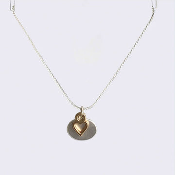 A chain necklace with a gold heart outline pendant over a silver oval pendant.