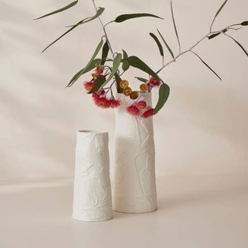 A tall cylinder shaped vase in white porcelain embossed with banksia flowers.