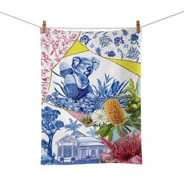 A cotton tea towel illustrated with a koala, house and flowers in a collage design is hanging from a rope with pegs.