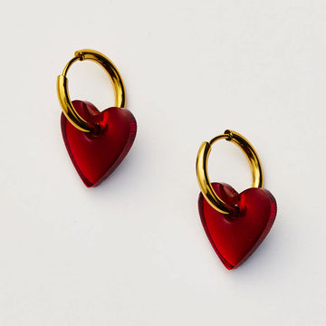 Heart-shaped red earrings with gold hoops on a light gray background.