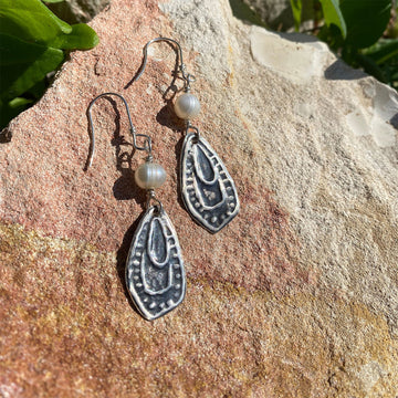 Silver earrings with pearl drops on a stone surface.