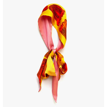 A silk twilly scarf with peach pink on one side and a yellow and orange design on the other.