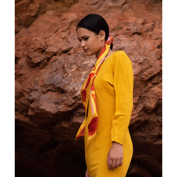 A silk twilly scarf with peach pink on one side and a yellow and orange design on the other.