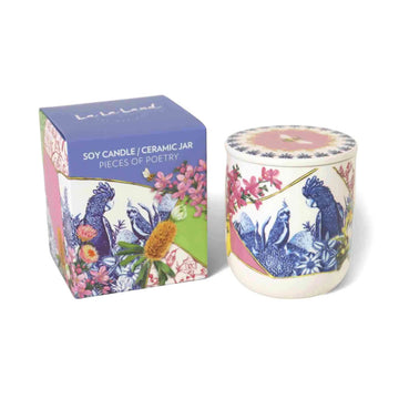 A candle in a ceramic jar next to a packaging box illustrated with birds and flowers.