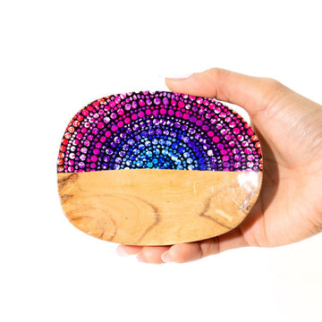 Hand holding a wooden trinket tray with a colorful dot pattern on a white background.