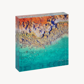 A square acrylic desk block printed with a photo of Dinosaur Land with rocks and the ocean.