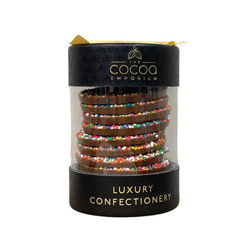 A small cylinder container filled with sprinkle covered disc shaped chocolates.