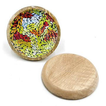 A wooden round trinket dish is pictured twice, one showing the patterned inside with artwork by Patricia Multa and the other upside down showing the base.