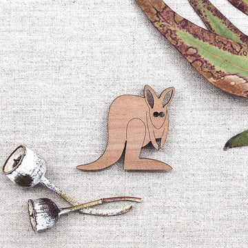 A wooden magnet shaped like a kangaroo with gum leaves in the background.