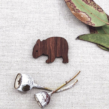 A wooden magnet shaped like a wombat with gum leaves in the background.