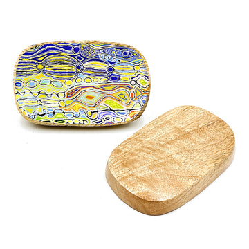 A wooden oblong trinket dish is pictured twice, one showing the patterned inside with artwork by Judy Watson and the other upside down showing the base.