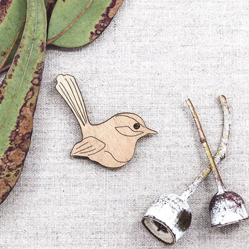A wooden magnet shaped like a fairy wren with gum leaves in the background.