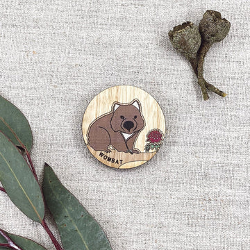 A round wooden magnet illustrated with a wombat with gum leaves in the background.