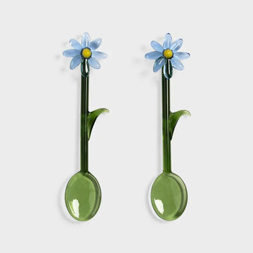 Two green glass spoons with blue floral ends on a white background.