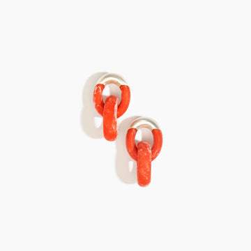 A pair of earrings made up of two hoops intertwined made from orange pink resin.