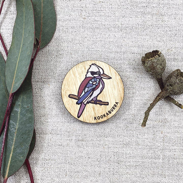 A wooden round magnet illustrated with a colourful kookaburra and gum leaves in the background.