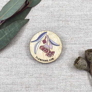 A wooden round magnet illustrated with a flowering gum with gum leaves in the background.