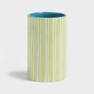 Cylindrical ceramic vase with green and blue striped pattern on a light gray background.