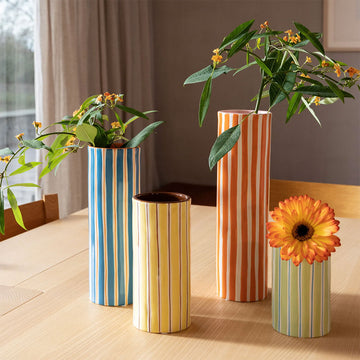 Cylindrical vase with orange and white vertical stripes on a light gray background.