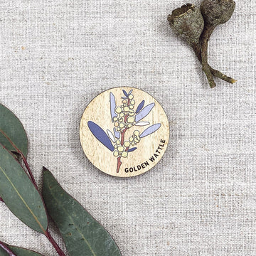 A wooden round magnet illustrated with a golden wattle flower.