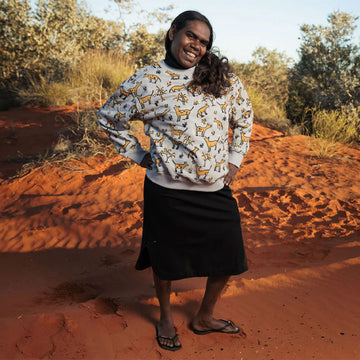 Gray sweater with yellow dingo pattern on a hanger against a gray background.