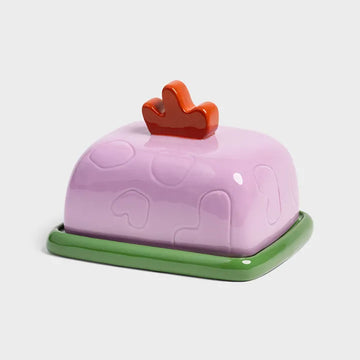 Pink butter dish with a red handle and green base on a white background.
