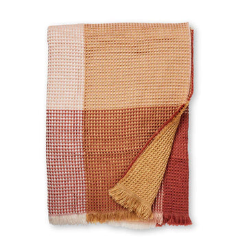 A folded up throw with a waffle pattern and printed with large checks in shades of pink and orange.