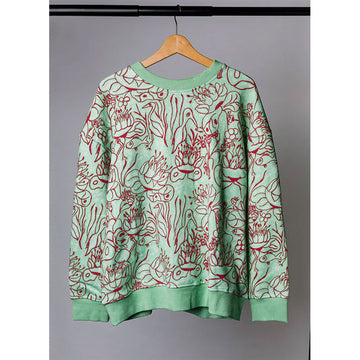 Green sweatshirt with red abstract patterns on a hanger against a gray background.