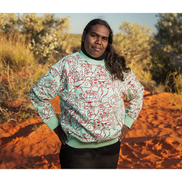Green sweatshirt with red abstract patterns on a hanger against a gray background.