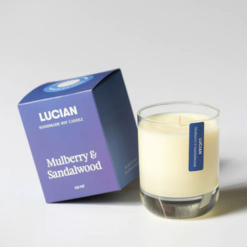 A glass candle next to a blue purple box with the text 'Lucian Mulberry & Sandalwood'.