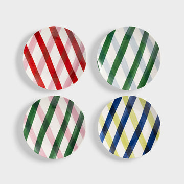 Four round ceramic plates with colorful diagonal stripe patterns on a light gray background.