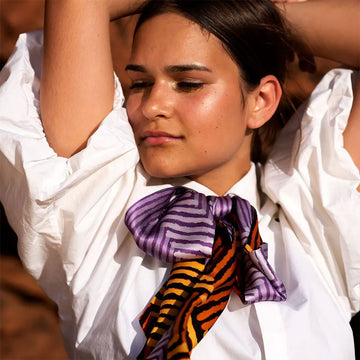 A twilly style scarf printed with a chevron pattern in orange on one side and a chevron pattern in purple on the other side.