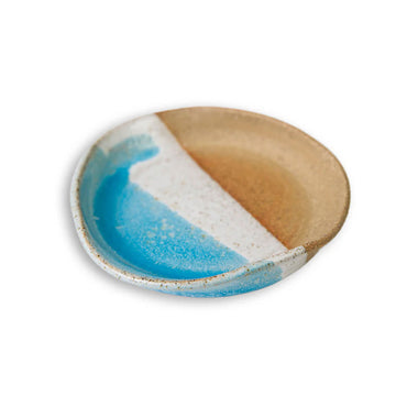 A handmade ceramic dish in brown with half covered in blue and white paint.