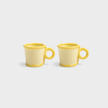 Two yellow ceramic mugs on a light gray background.