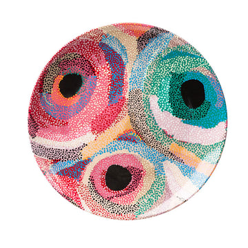 A round ceramic plate printed with artwork by Marianne Burton in red, blue, black and green.