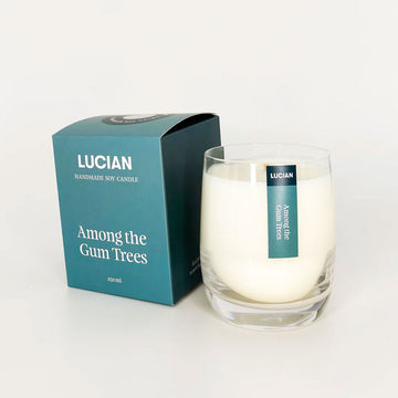 A glass candle next to a green blue box with the text 'Lucian Among the Gum Trees'.