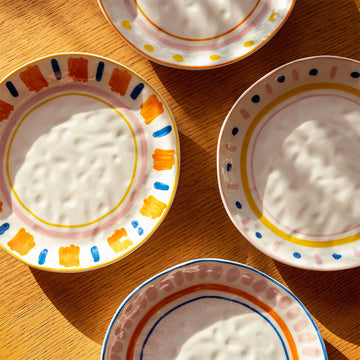 Four round ceramic plates pictured each featuring a different coloured stripe and spot border.