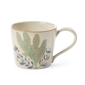 A ceramic mug painted wit a blue flower and large green leaf.