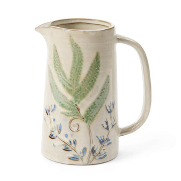 A ceramic jug painted with blue flowers and a large green leaf.