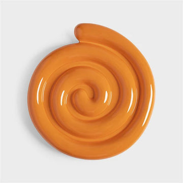 A ceramic trivet shaped like a spiral in orange.