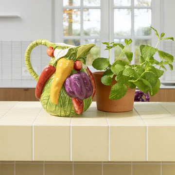 Ceramic pitcher with embossed vegetable design on a white background.