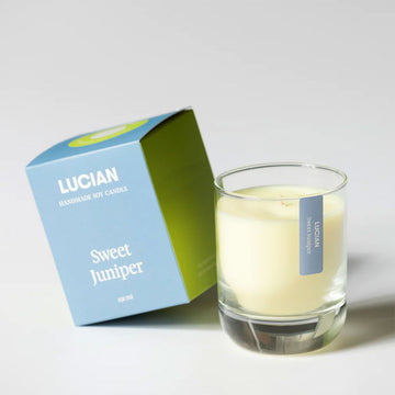 A glass candle next to a blue box with the text 'Lucian Sweet Juniper'.