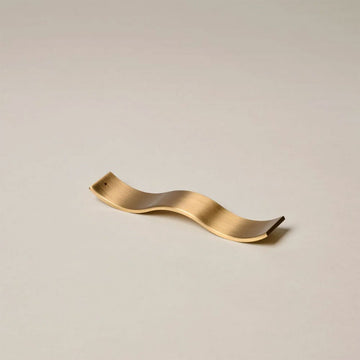 Brass wavy decorative object on a beige background.