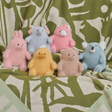 Six fluffy soft toys in different animals shapes on a green and white knitted blanket.
