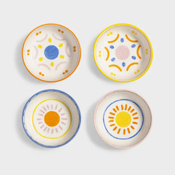 Top down view of four ceramic bowls with colourful sun designs on a light grey background.