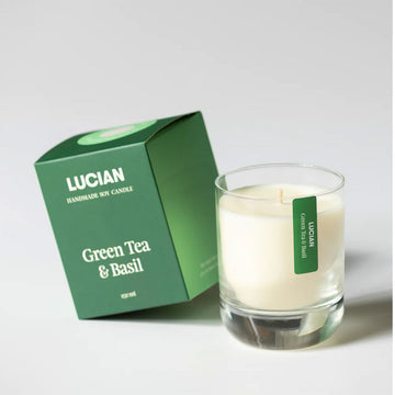 A glass candle next to a green box with the text 'Lucian Green Tea and Basil'.