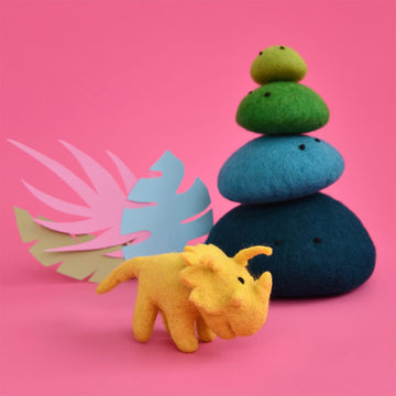 A yellow triceratops made from felt standing next to a stack of green and blue felt rocks.