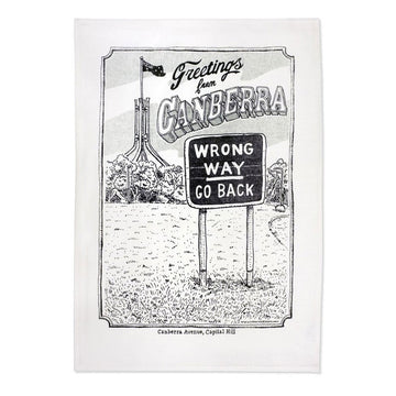 A white linen tea towel with a black and white line drawing of Parliament House and a sign that says 'Wrong Way Go Back' and 'Greetings from Canberra'.